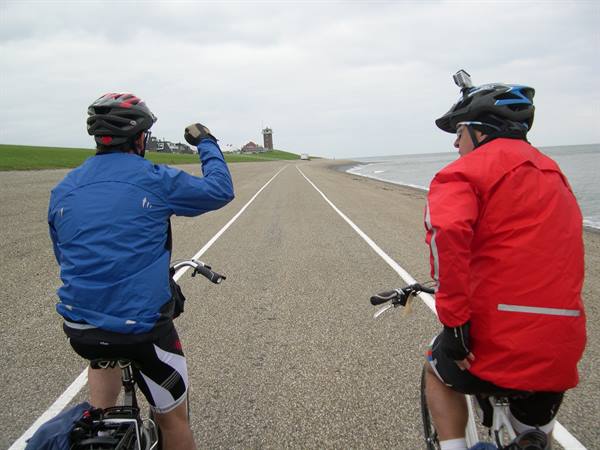 Two cyclists ride along a coastal road under gray sky, sea on right