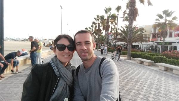 Couple posing on palm-lined promenade with tiled pavement and strollers
