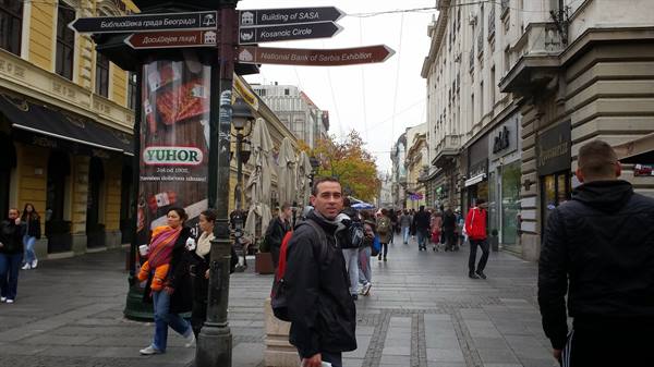 Man with backpack on busy pedestrian street, directional signs and shop signs, Belgrade