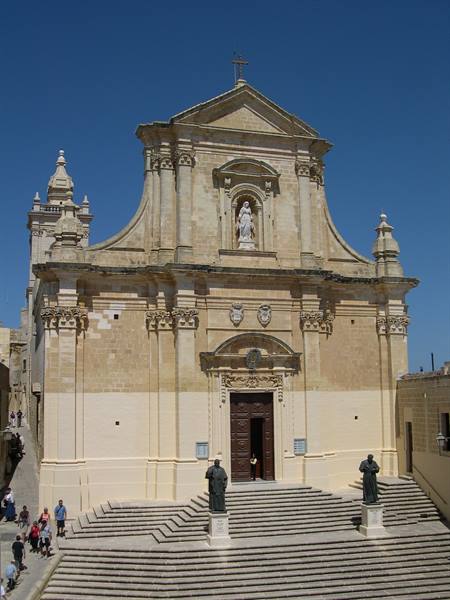 Baroque limestone church with wide staircase and statues, tourists under blue sky