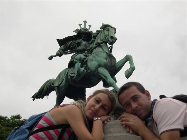 Couple of tourists leaning on the base of a bronze equestrian samurai statue