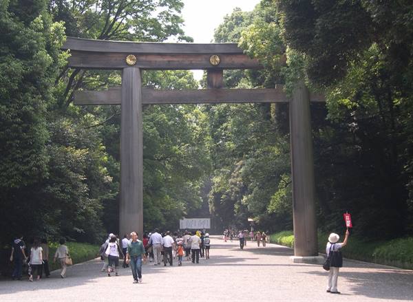 Tourists walk beneath the giant wooden torii gate of Meiji Shrine among trees