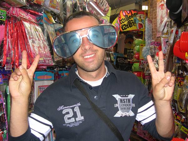 Tourist in giant novelty sunglasses gives peace signs in a Japanese gadget shop