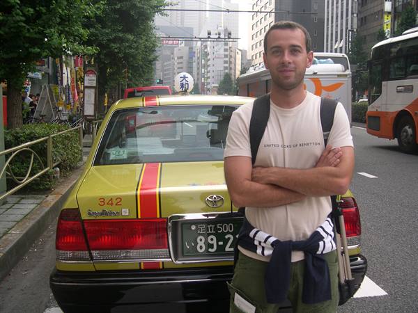 Young man in white t-shirt standing beside a yellow taxi in Tokyo