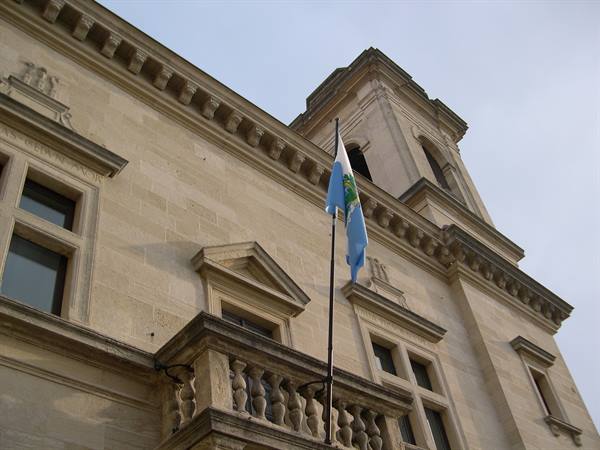 San Marino Public Palace, white-blue flag waving over limestone balcony under grey sky