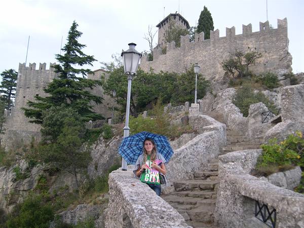 Tourist with umbrella beneath the crenellated Guaita fortress walls, San Marino