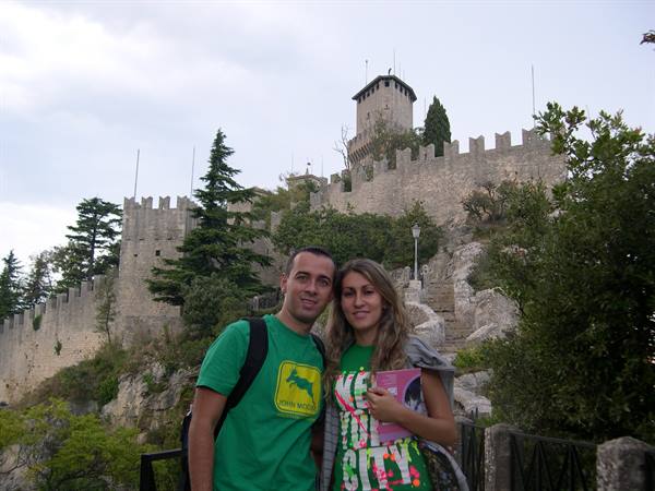 Smiling couple in front of the crenellated Guaita tower in San Marino