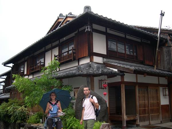Tourists with umbrella in front of traditional wooden house with red lanterns