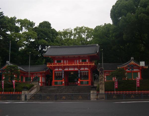 Red gate of Yasaka Shrine in Kyoto surrounded by green trees under grey sky