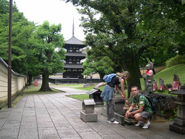 Tourists drink at a stone fountain near a wooden pagoda among trees