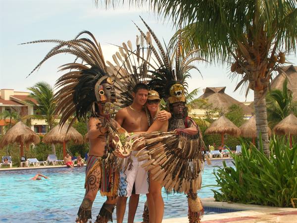 Tourists with two Aztec dancers in feathered costumes by the pool