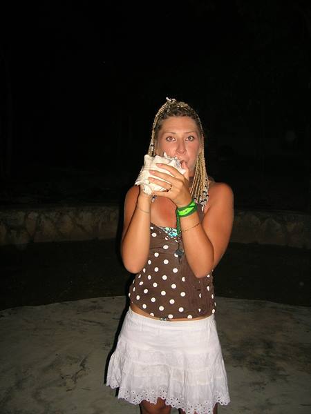 Girl with braids blowing a large conch shell at night on concrete