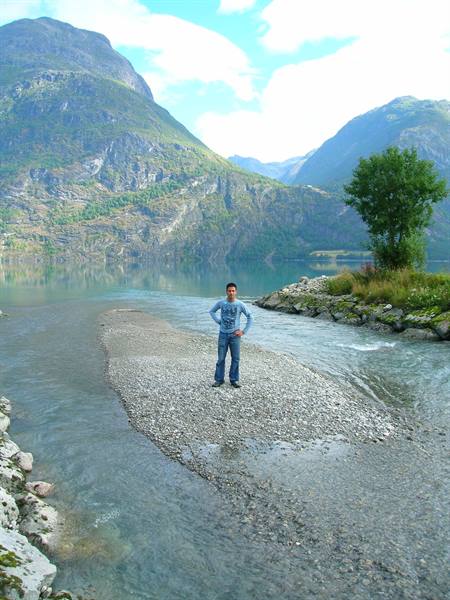 Tourist standing on a gravel bar between clear waters, mountains reflected on the lake