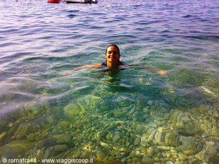 Woman swimming in clear sea with visible pebbles and a boat behind