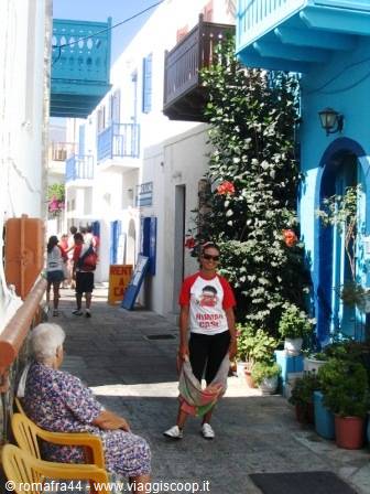 Woman standing and elderly lady sitting in a Greek alley with white houses and blue balconies