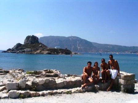 Four friends sitting on a stone wall in front of Gallinara island, Alassio
