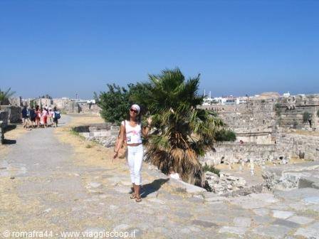 Tourist in white walks among ancient stone ruins, palm tree and blue sky