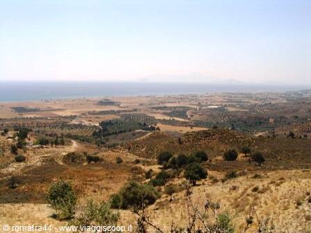 Dry hills with shrubs and olive groves toward the hazy sea and coastline