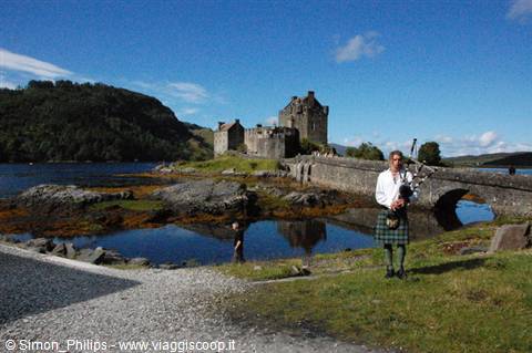 Bagpiper in kilt playing in front of Eilean Donan Castle