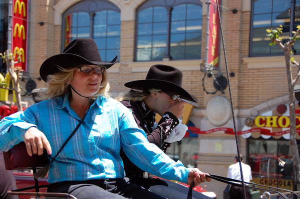 Two women in black cowboy hats drive a horse carriage through San Francisco street