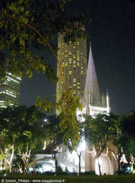 St Andrew's Cathedral lit up at night among skyscrapers and trees in Singapore