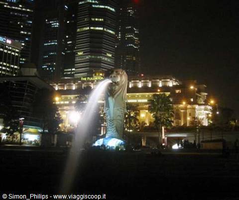 The Merlion statue spouts water into Singapore's bay, among illuminated skyscrapers