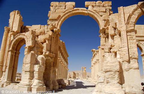 Monumental stone arch among the ruins of Palmyra, under blue sky