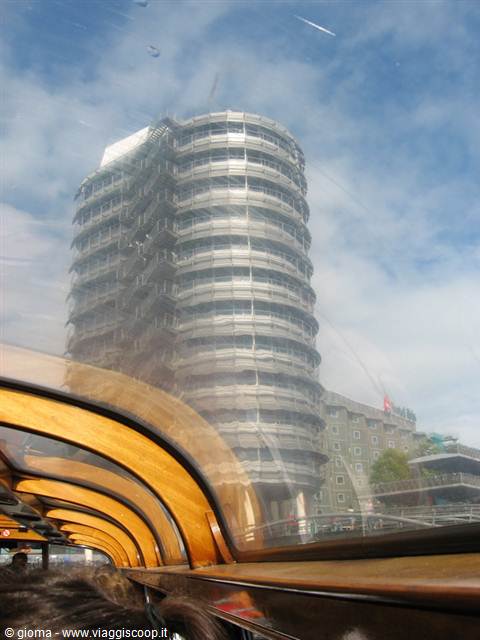 Cylindrical 1950s tower seen from the tourist boat, sky reflecting on the glass