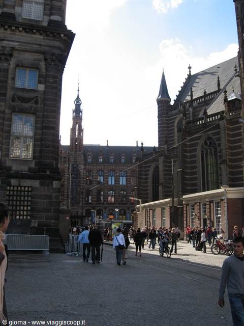 Tourists walk across a square by a dark brick church and historic buildings