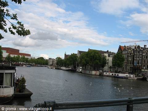 Amsterdam canal with Dutch houses, houseboats and gulls under clouds