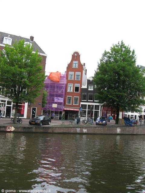 Amsterdam canal houses with purple scaffolding, cars and trees along the quay