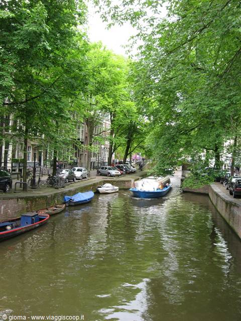 Boats on Amsterdam canals between green trees and brick houses