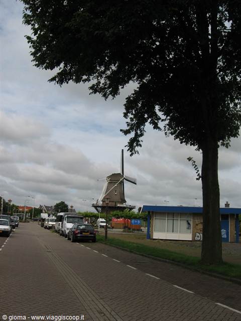 Brick windmill beside a street with parked cars and blue kiosk