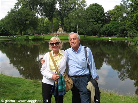 Smiling couple in front of the Vondelpark pond, green trees and statue behind