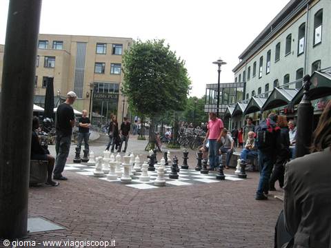 Giant street chessboard, people playing chess among buildings and bicycles