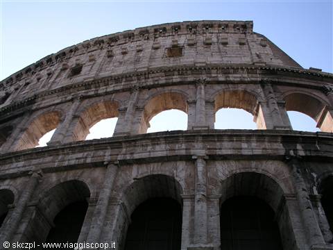 Travertine arches of Rome's Colosseum backlit against blue sky