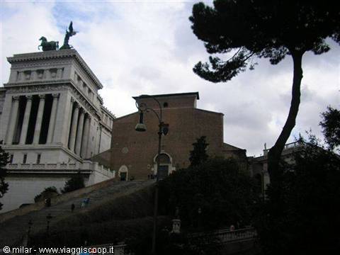 White Vittoriano monument and brick church under cloudy sky in Rome