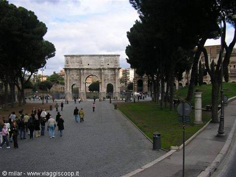 Tourists walk toward the Arch of Constantine, with the Colosseum among trees