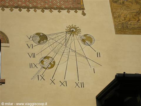 Painted sundial with golden sun and globes on ochre wall
