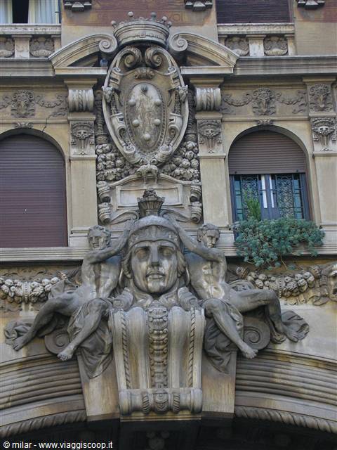 Stone sculptures with face, nude figures and crest on Liberty-style building facade