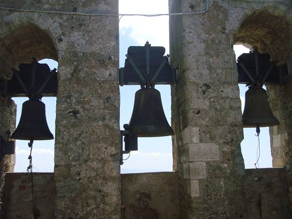 Three bronze bells in a stone bell tower, blue sky behind