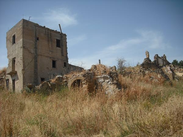 Dilapidated stone farmhouse among dry grass, blue sky