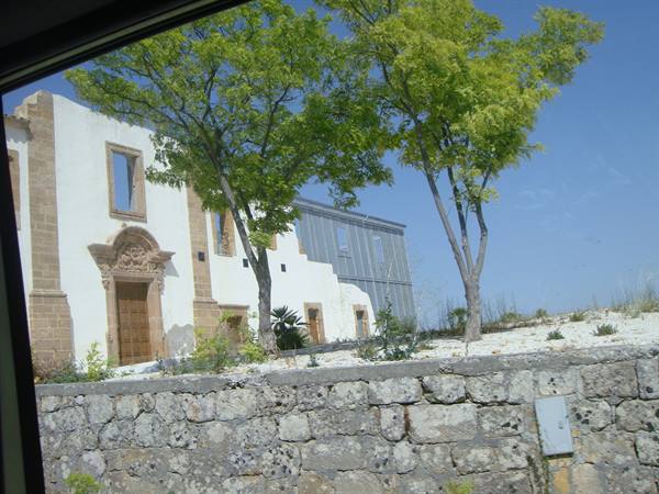 White church with carved portal and green trees, seen from the bus