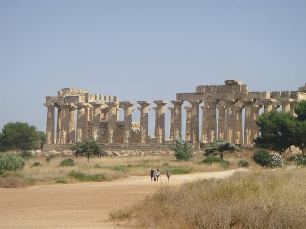 Tourists walk toward the Doric temple ruins of Selinunte among dry grass