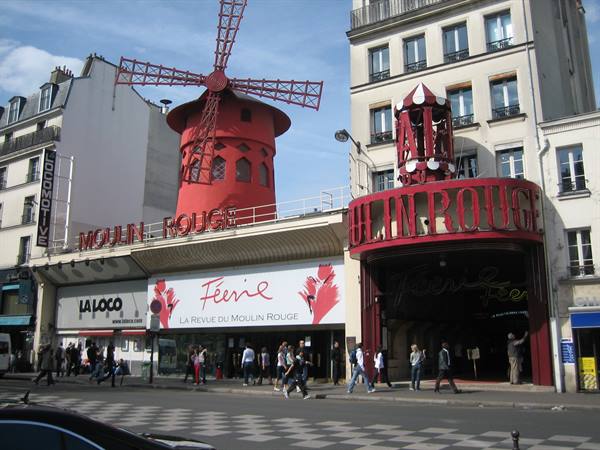 Tourists walk past the Moulin Rouge in Paris, with its famous red windmill