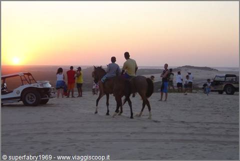 Riders on sand dunes at sunset, buggies and tourists around