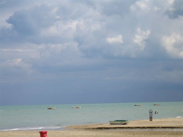green boat moored on the sand, red bucket in the foreground, cumulus clouds over the sea