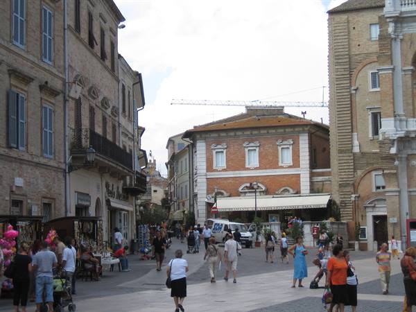 People strolling through Piazza del Popolo in Fermo among historic brick buildings