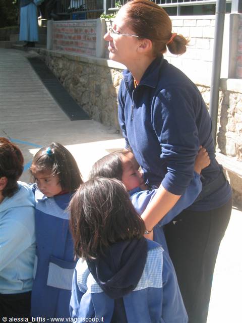 Volunteer in blue sweater hugging schoolchildren in uniforms in sunlight