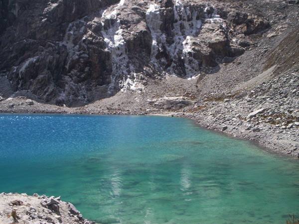Turquoise alpine lake surrounded by scree slopes and rock walls with snow patches